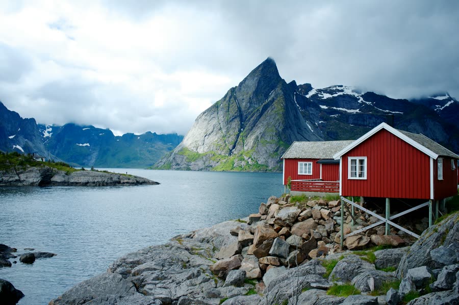 A red wooden cabin at the edge of a Norwegian fjord