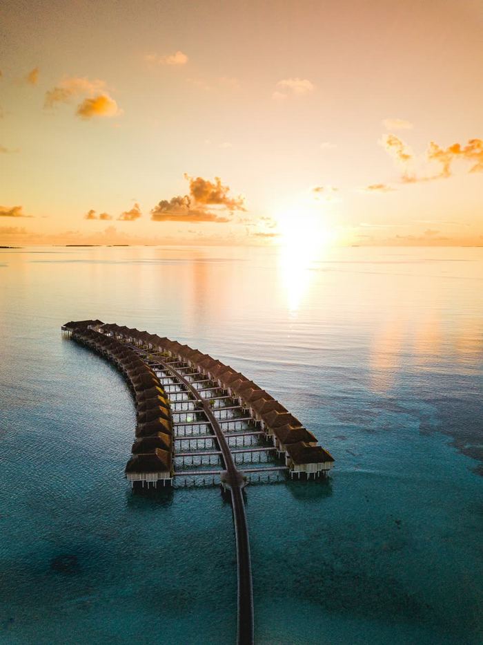 A wooden jetty stretching over calm water at sunset in the Maldives