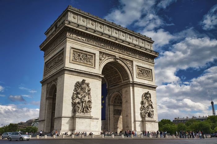 The Arc de Triomphe under blue sky with the Eiffel Tower in the distance