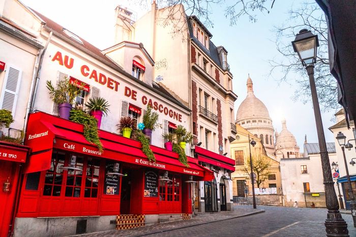 Montmartre street with a red brasserie and the domes of Sacré-Cœur behind